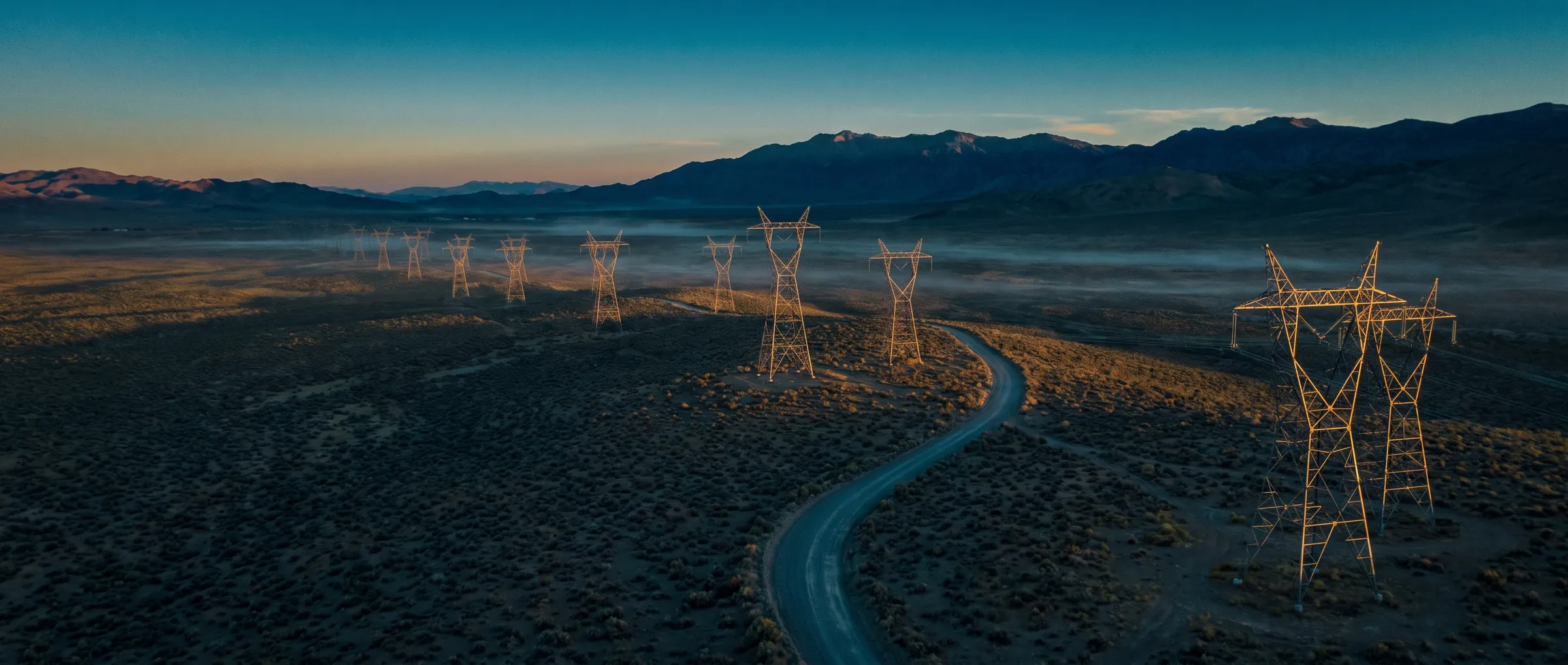 Aerial view of a logistics and energy corridor at dusk, teal-lit under a low sun